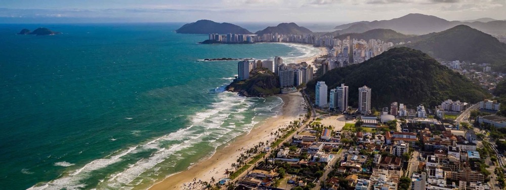 Vista aérea da praia de Pitangueiras, no Guarujá, com o mar à esquerda e os prédios da orla à direita